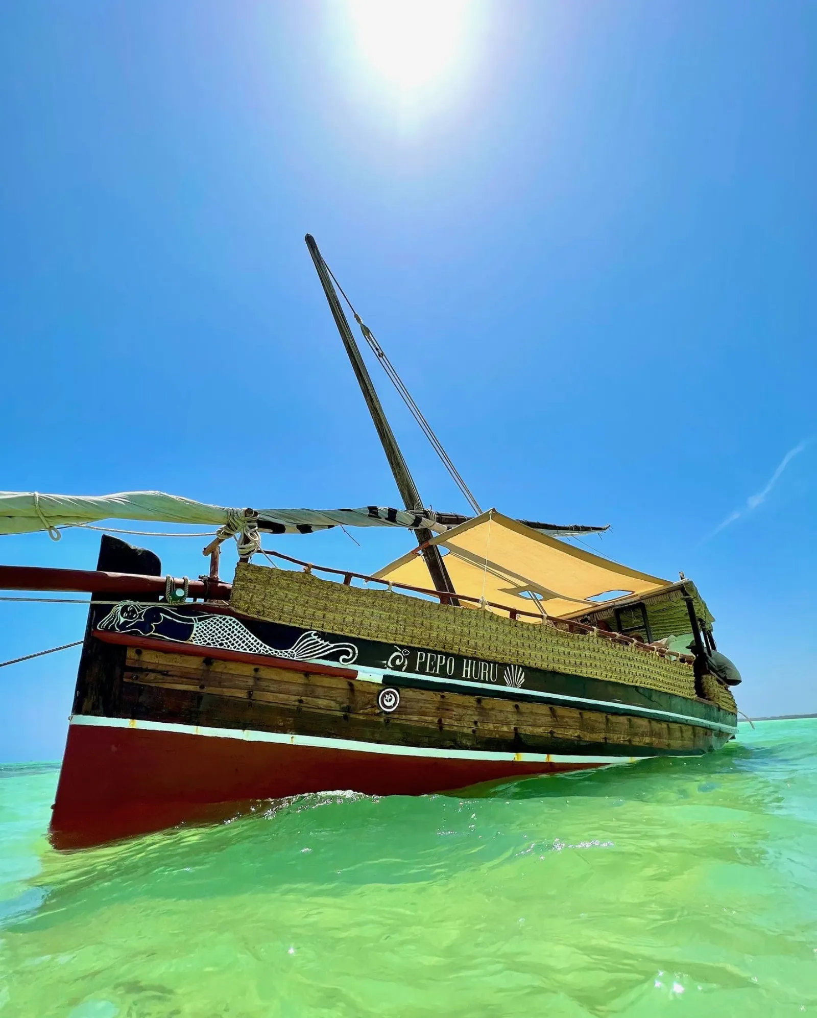 A traditional wooden dhow sailing across the turquoise waters of Mida Creek at sunset