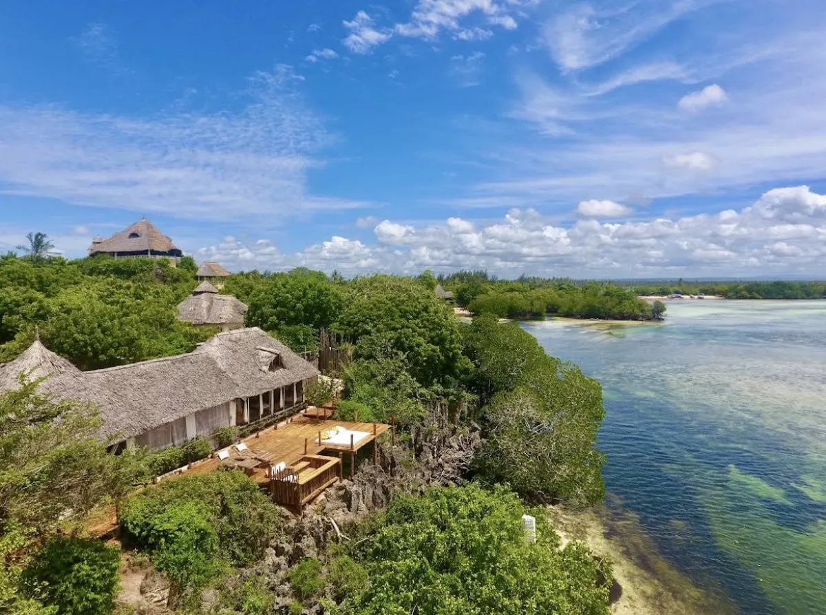 Aerial view of the thatched lodges of The Rock and Sea on their coral cliff above the turquoise channel of Mida Creek
