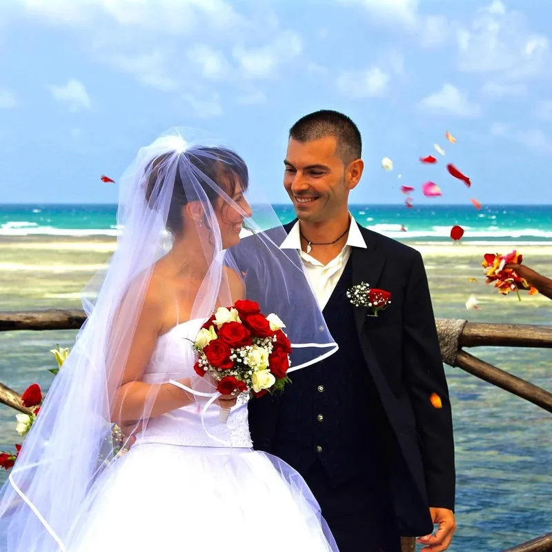 A couple beneath a flower-dressed arch on the sand at the edge of Mida Creek