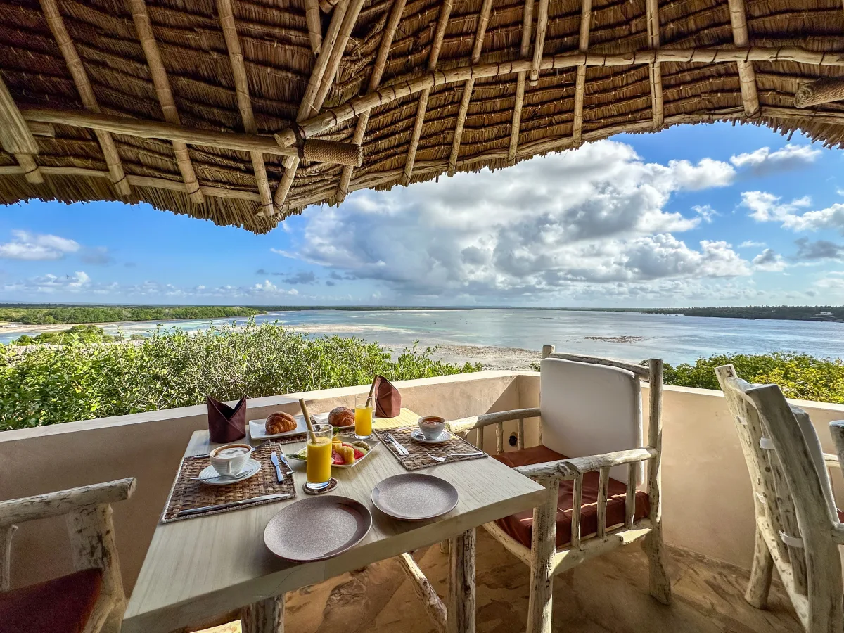 A table laid for breakfast under the makuti roof, open to the creek and the morning sky